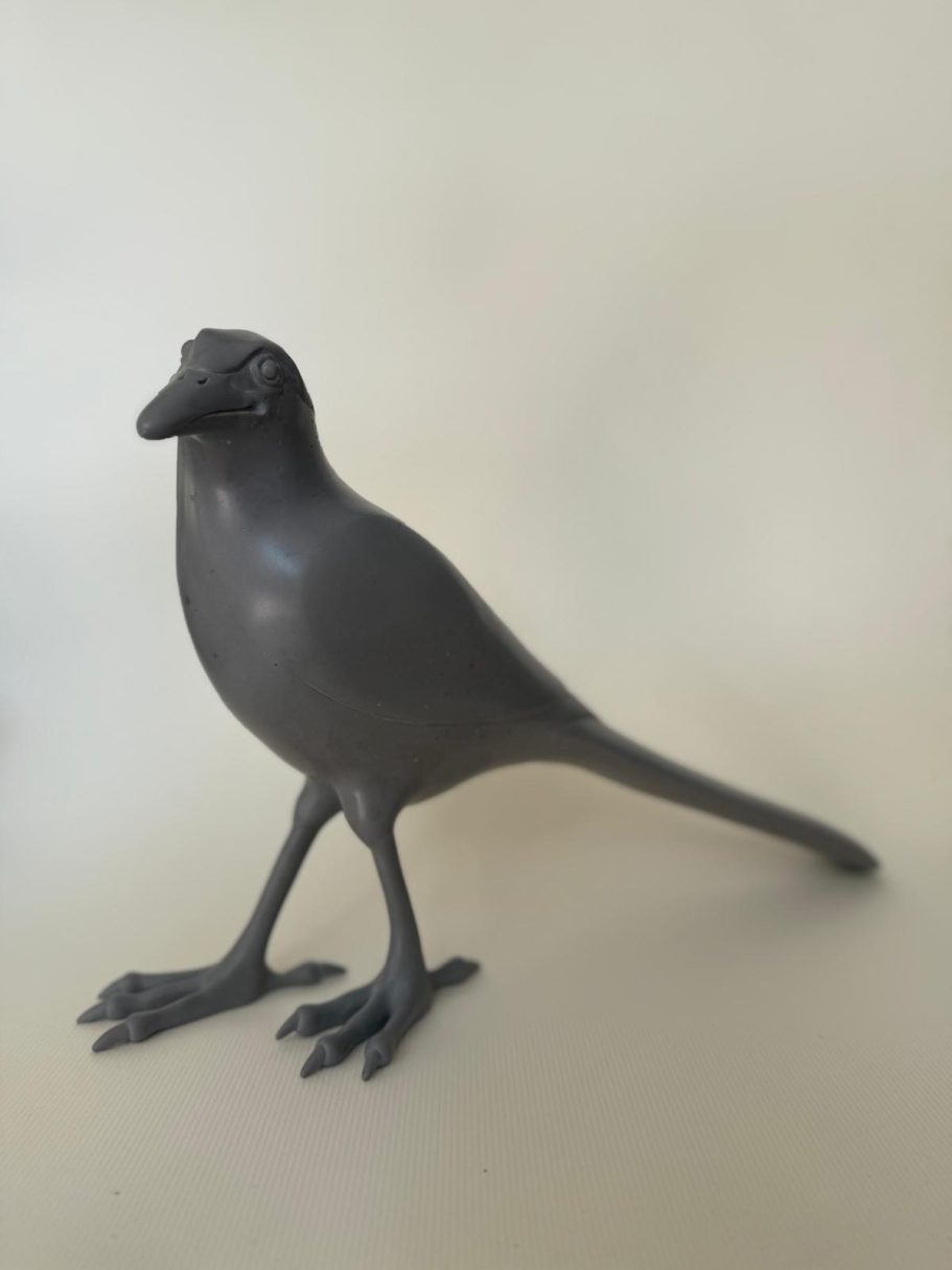 Oiseau en résine noir sur fond clair, debout avec un corps élancé et des pattes fines.